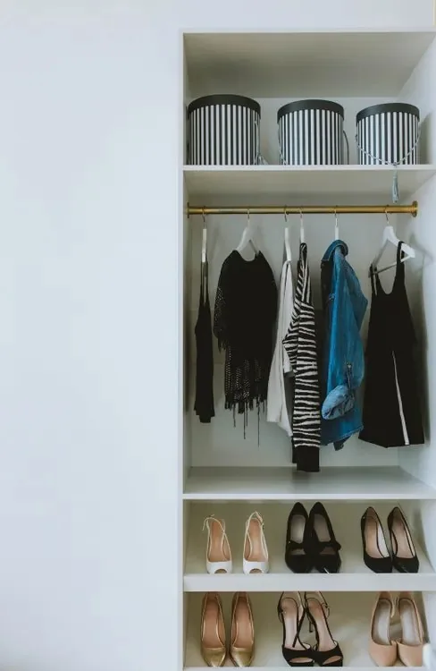 A tidy closet with storage boxes on the top shelf, clothes on hangers, and shoes arranged in rows