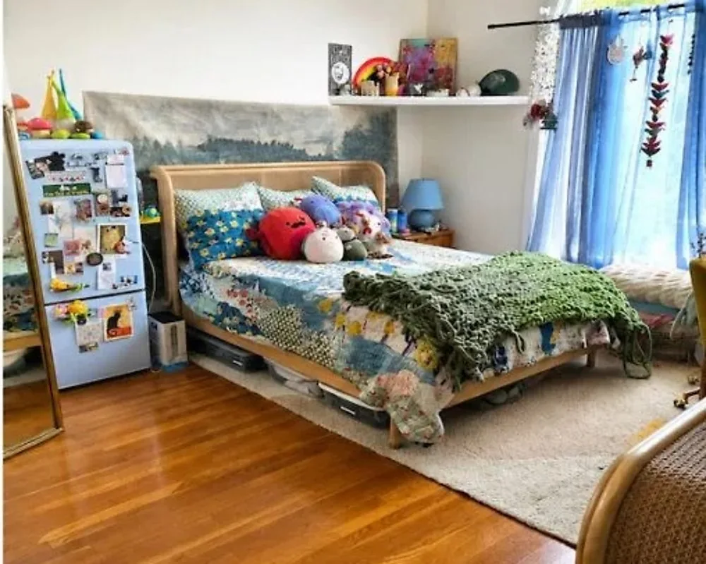 After: the same bedroom tidied, with the bed made in a patchwork quilt, the same blue curtains and magnet covered fridge, and a clear wood floor