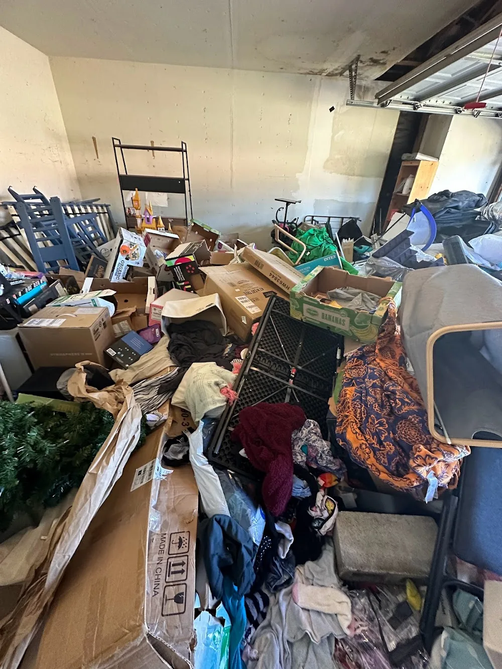 Inside a packed garage mid-cleanout, with boxes, bags, and household items being sorted